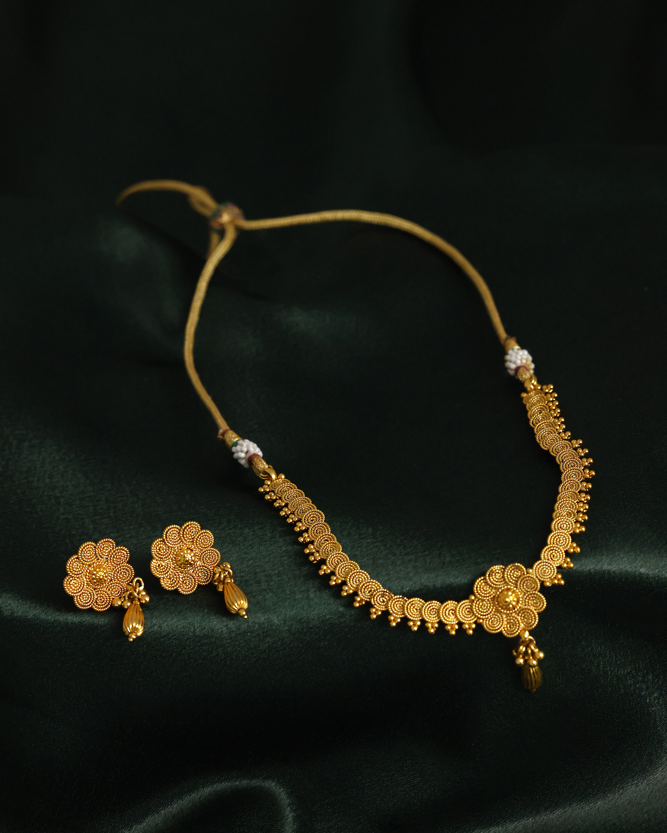 Traditional gold necklace with matching stud earrings on dark green fabric