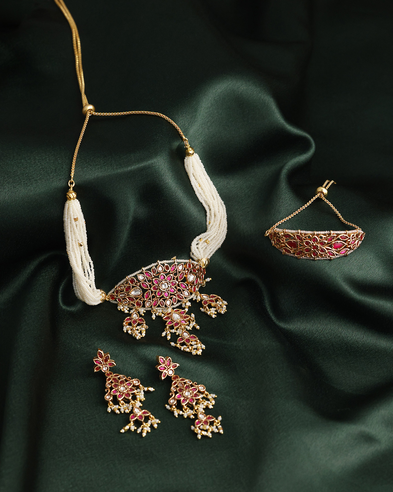 Gold and white beaded necklace with matching earrings and ring on dark green satin fabric